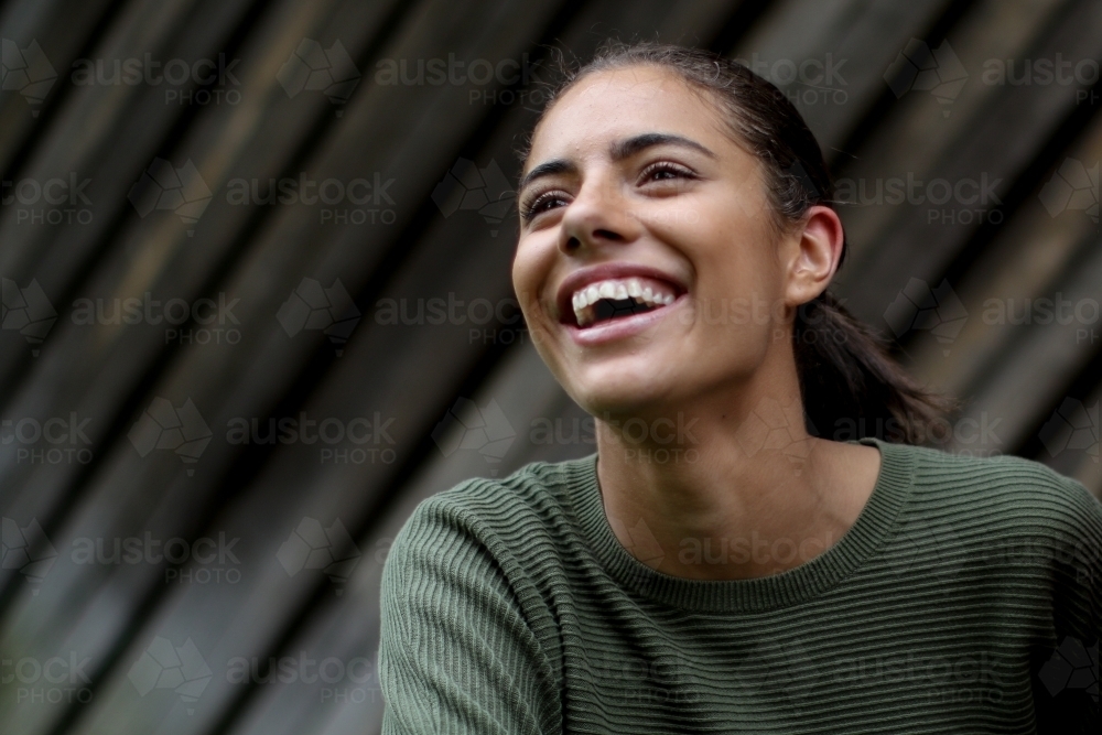 Young Fijian woman laughing in front of textured wooden panels - Australian Stock Image