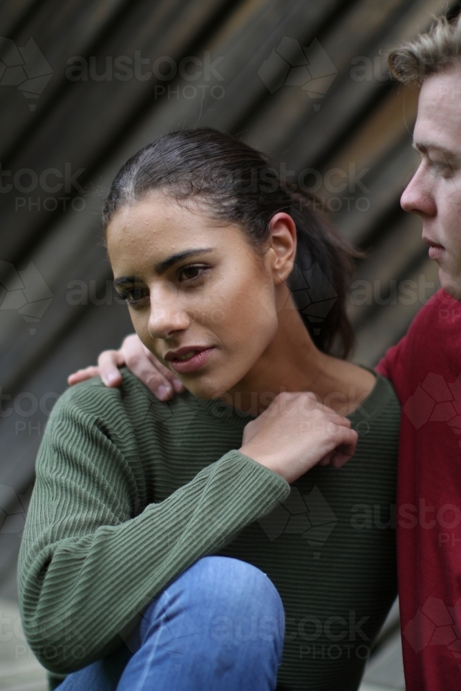 Young Fijian woman looking away as young caucasian man comforts her - Australian Stock Image