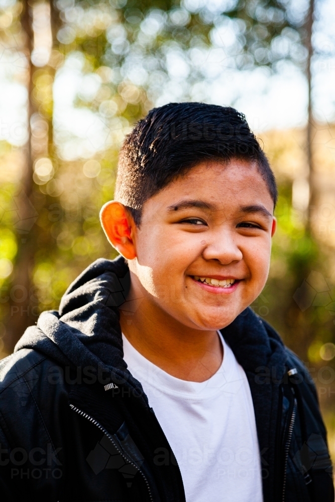 Young Filipino boy in leather jacket smiling in bushland - Australian Stock Image