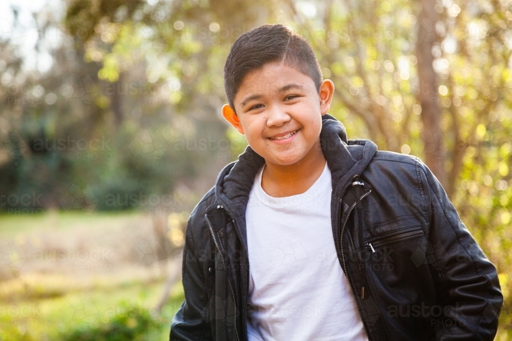 Young Filipino boy in leather jacket smiling in bushland - Australian Stock Image