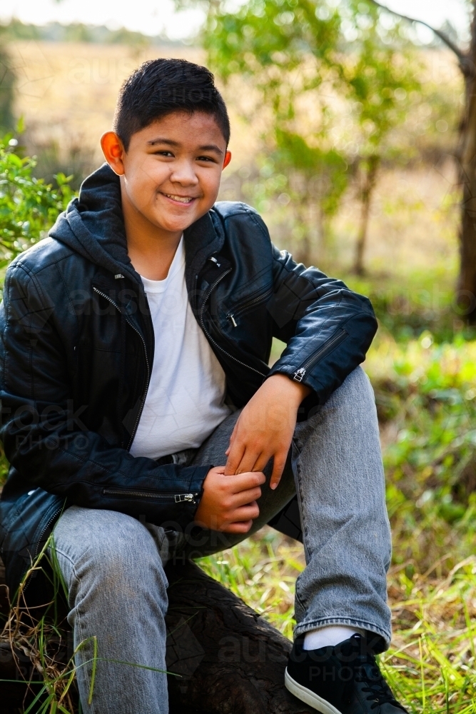 Young Filipino boy in leather jacket smiling in bushland - Australian Stock Image