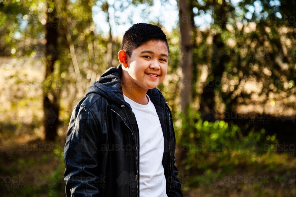 Young Filipino boy in leather jacket smiling in bushland - Australian Stock Image
