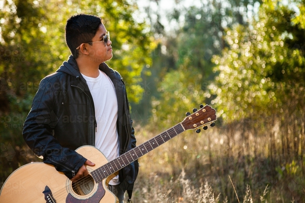 Young Filipino man holding musical instrument outside in nature - Australian Stock Image