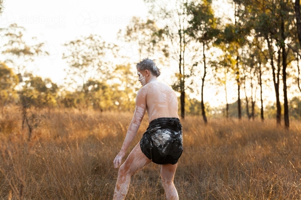 Young first nations australian man hunting through bushland at sunset - Australian Stock Image