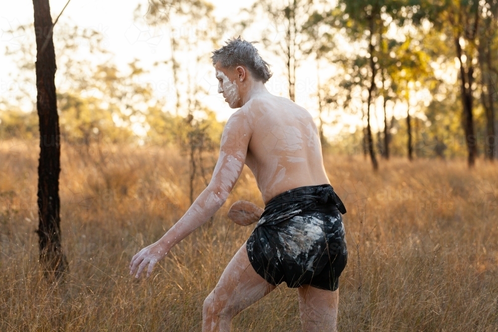 Young first nations australian man hunting through bushland at sunset - Australian Stock Image
