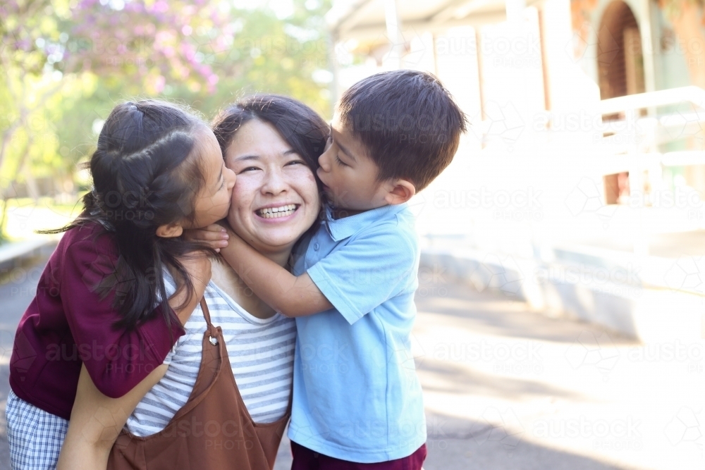 Young girl and boy in school uniform, hugging their mother. - Australian Stock Image