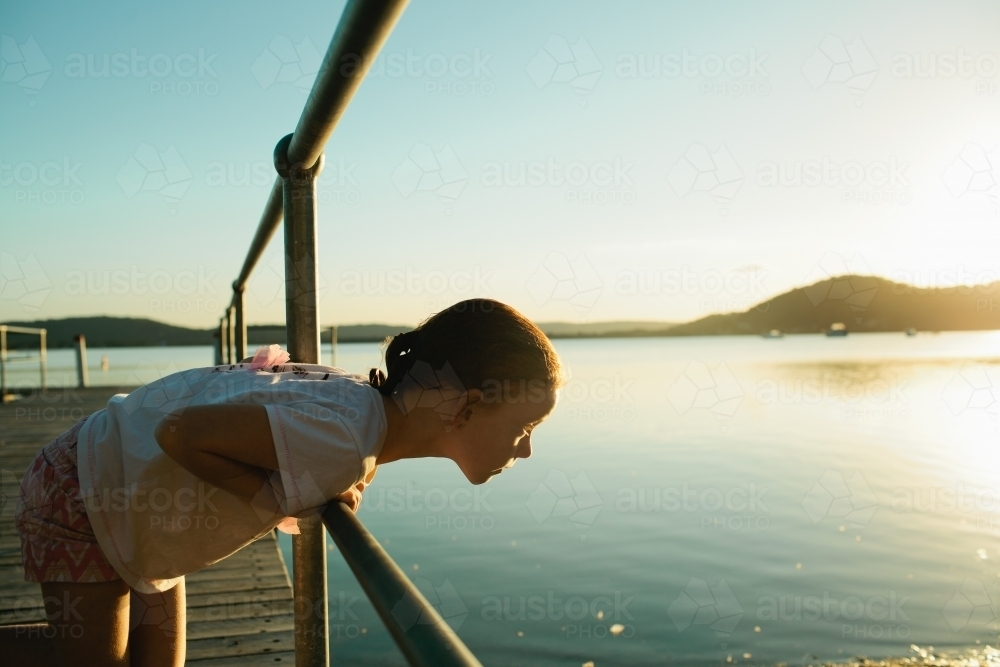 Young girl at a wharf leaning over looking at the water - Australian Stock Image