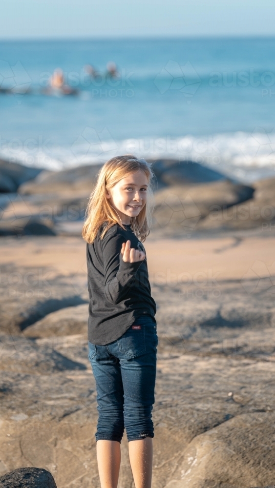 Young girl beckoning looking at camera on beach - Australian Stock Image