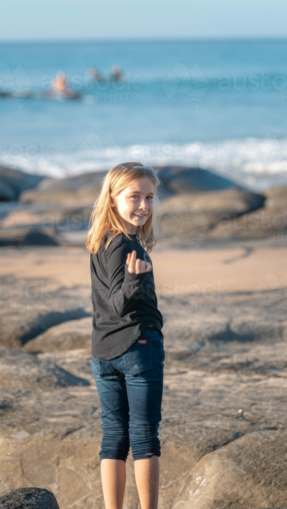 Young girl beckoning looking behind on beach - Australian Stock Image