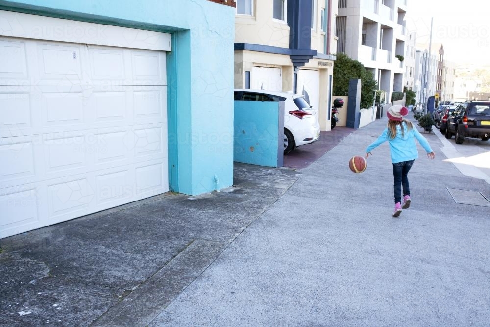 Young girl bouncing basketball down the street - Australian Stock Image