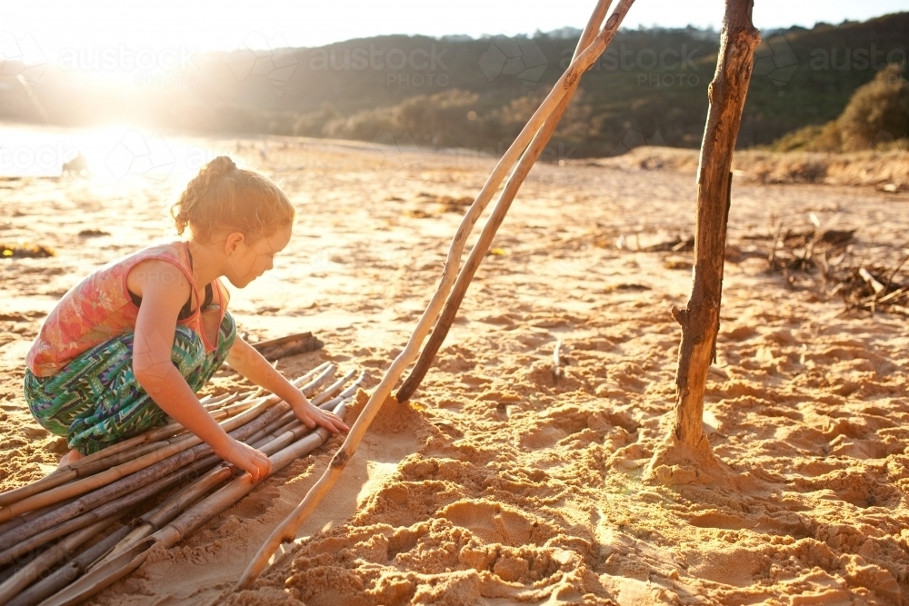 Young girl building a sculpture with driftwood at the beach - Australian Stock Image