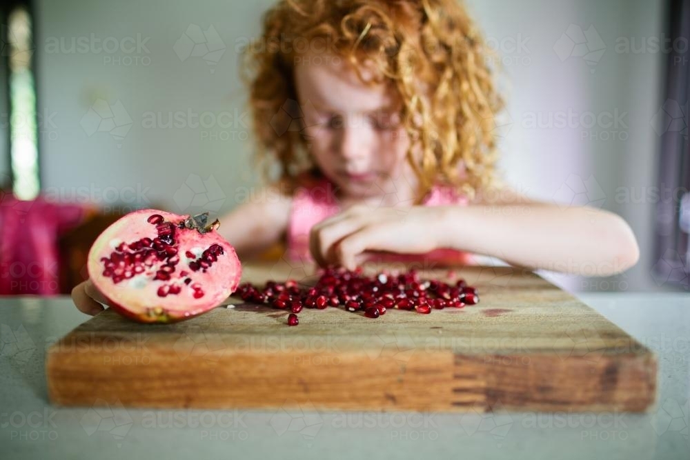 Young girl collecting pomegranate seeds in the kitchen - Australian Stock Image