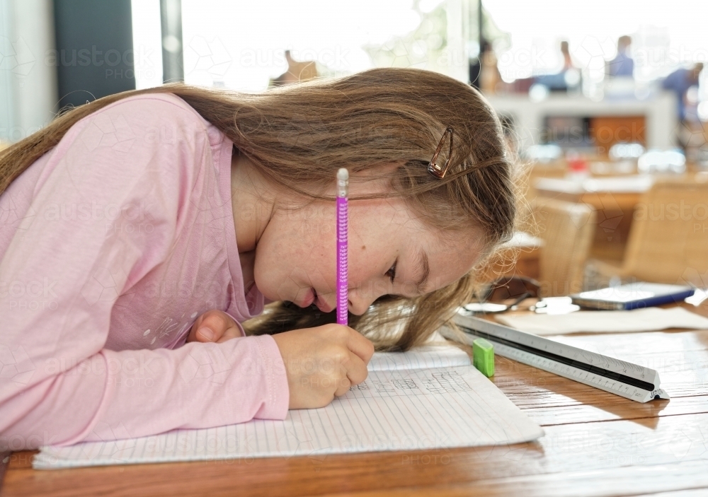 Young girl concentrating and writing in her homework book - Australian Stock Image