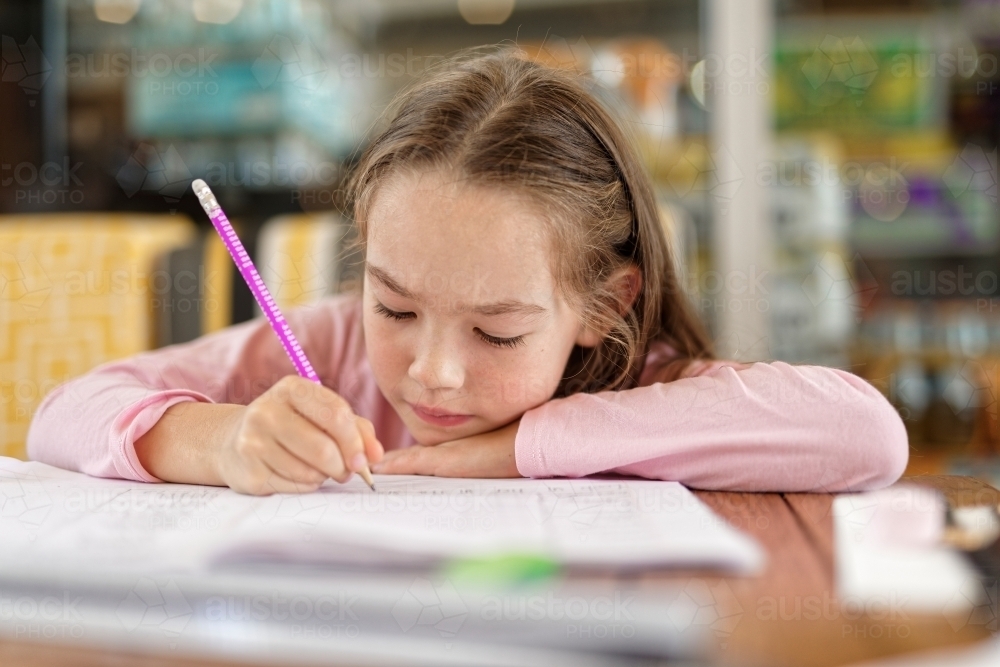 Young girl concentrating and writing sentences in her homework book - Australian Stock Image