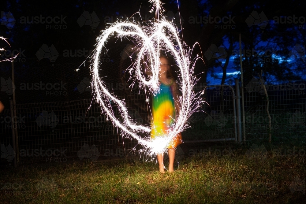 Young girl creating a heart shape with a sparkler at night - Australian Stock Image