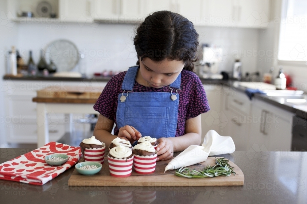 Young girl decorating cupcakes in kitchen at home - Australian Stock Image