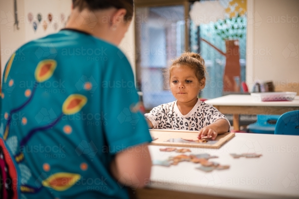 Young girl doing jigsaw puzzle with carer - Australian Stock Image