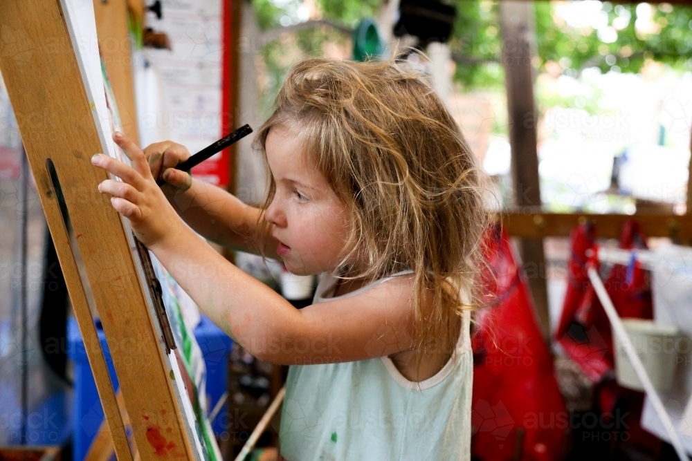 Young girl drawing using an easel at preschool - Australian Stock Image