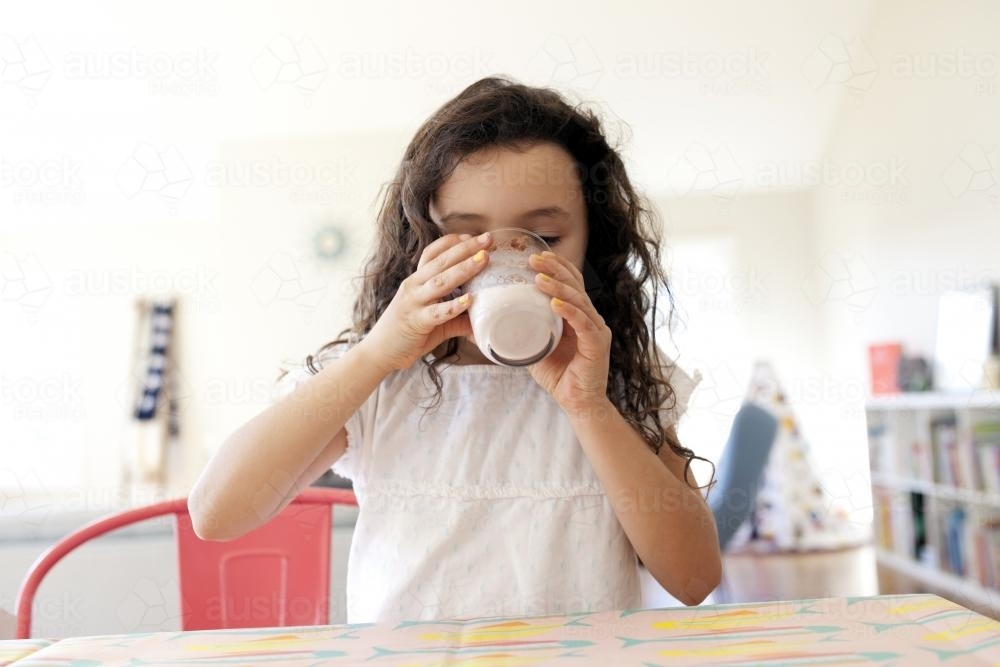 Young girl drinking chocolate milk at table - Australian Stock Image