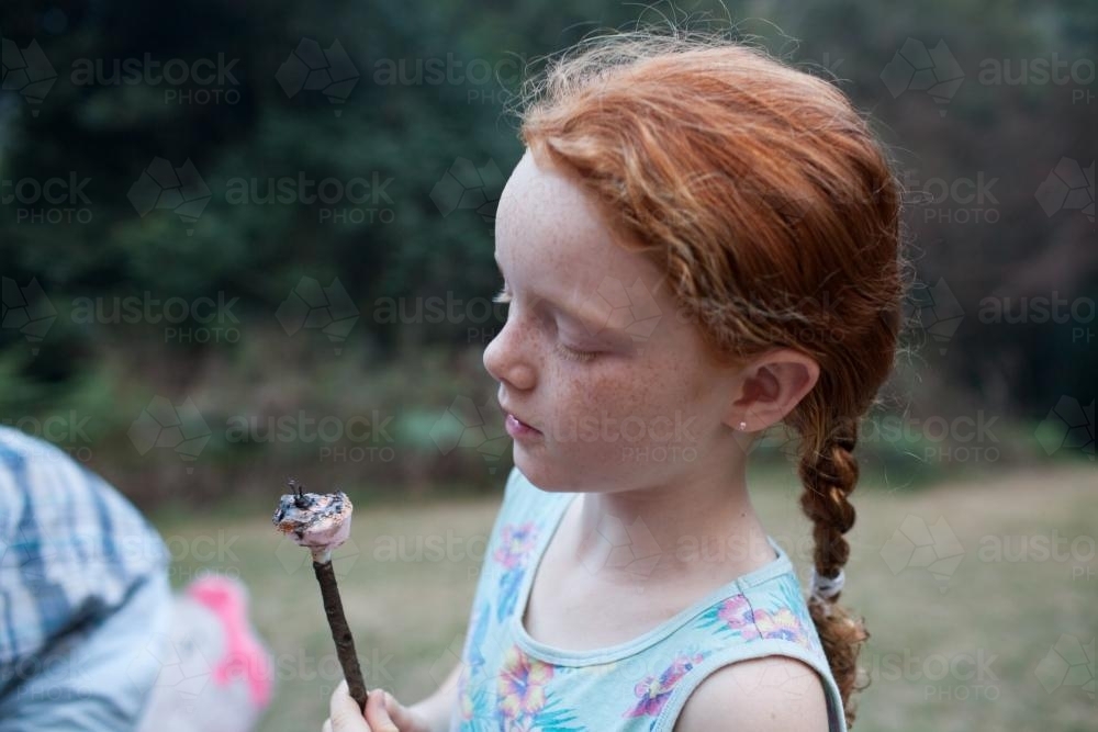Young girl eating a toasted marshmallow - Australian Stock Image