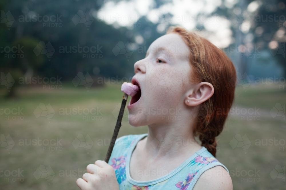 Young girl eating a toasted marshmallow - Australian Stock Image