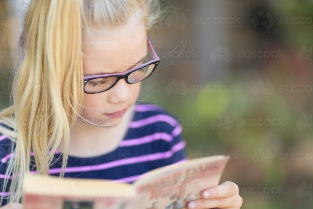 Young girl engrossed in reading a book - Australian Stock Image