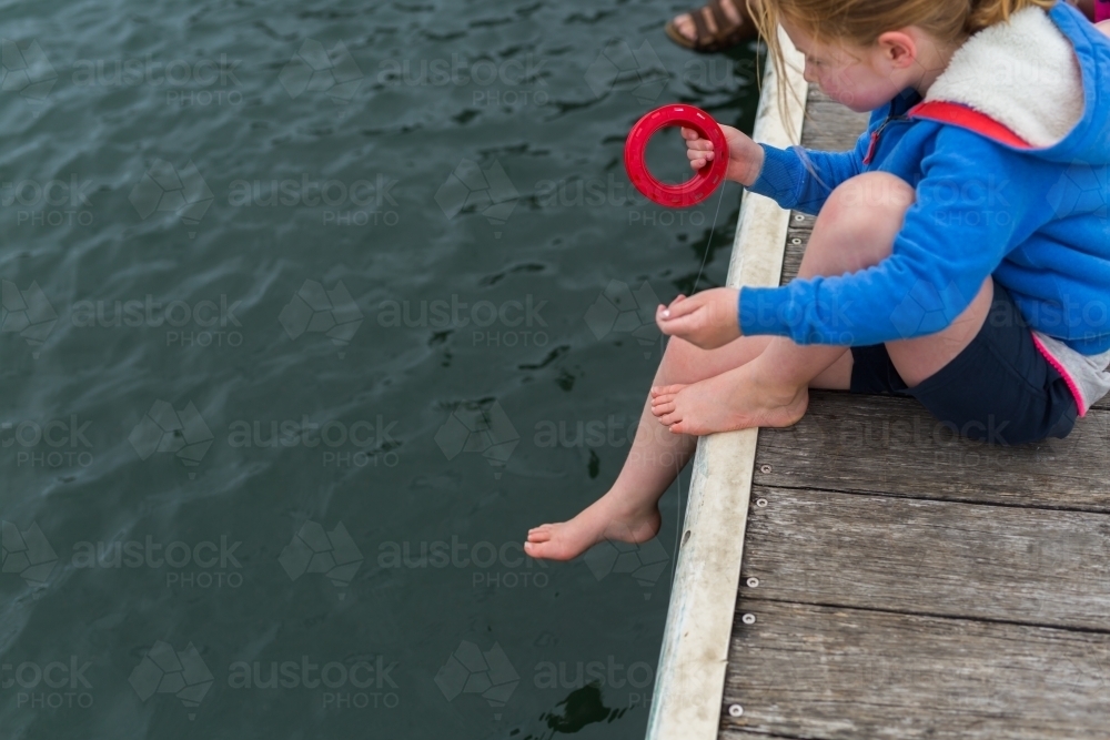 Young girl fishing off a wooden jetty with a hand reel - Australian Stock Image