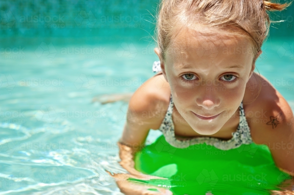 young girl floating in the pool with a green ball - Australian Stock Image