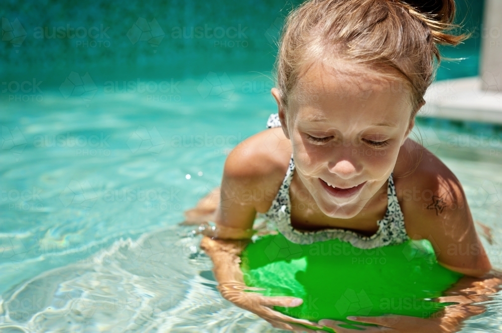 young girl floating in the pool with a green ball - Australian Stock Image