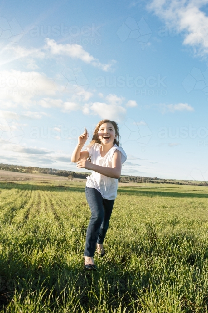 Young girl flying a paper aeroplane in a green farm paddock - Australian Stock Image