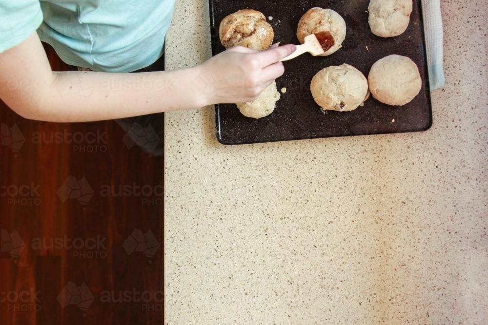 Young girl glazing hot cross buns - Australian Stock Image