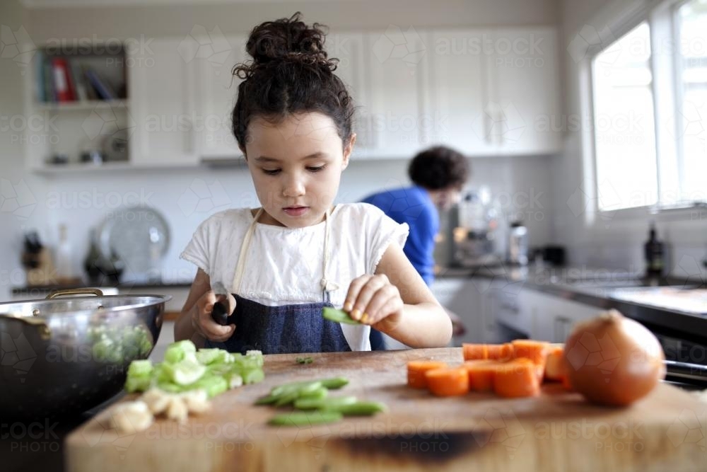 Young girl helping chop vegetables in kitchen - Australian Stock Image