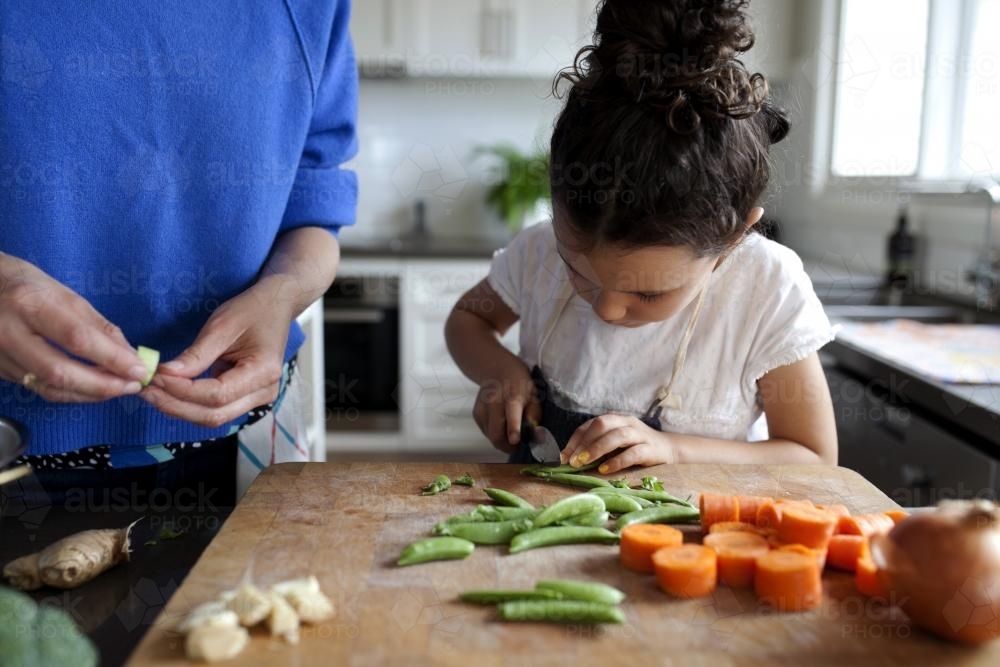 Young girl helping cook by chopping vegetables - Australian Stock Image