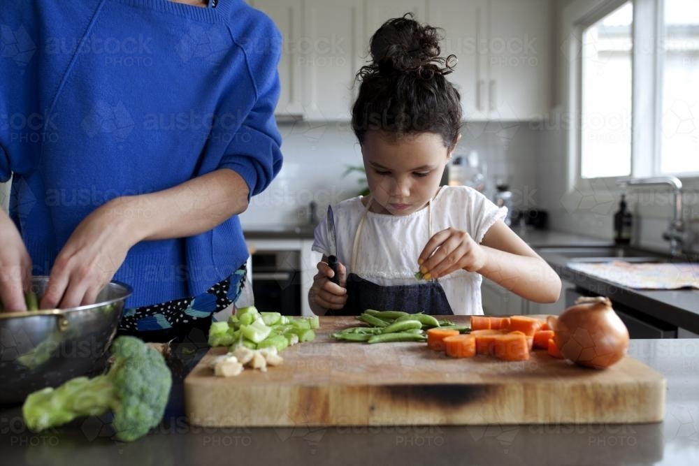 Young girl helping make dinner by cutting vegetables - Australian Stock Image