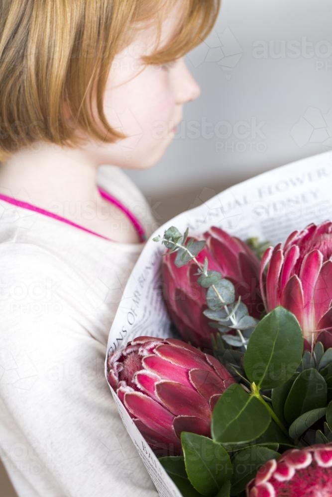 Young girl holding a bunch of red proteas and leaves wrapped in paper - Australian Stock Image