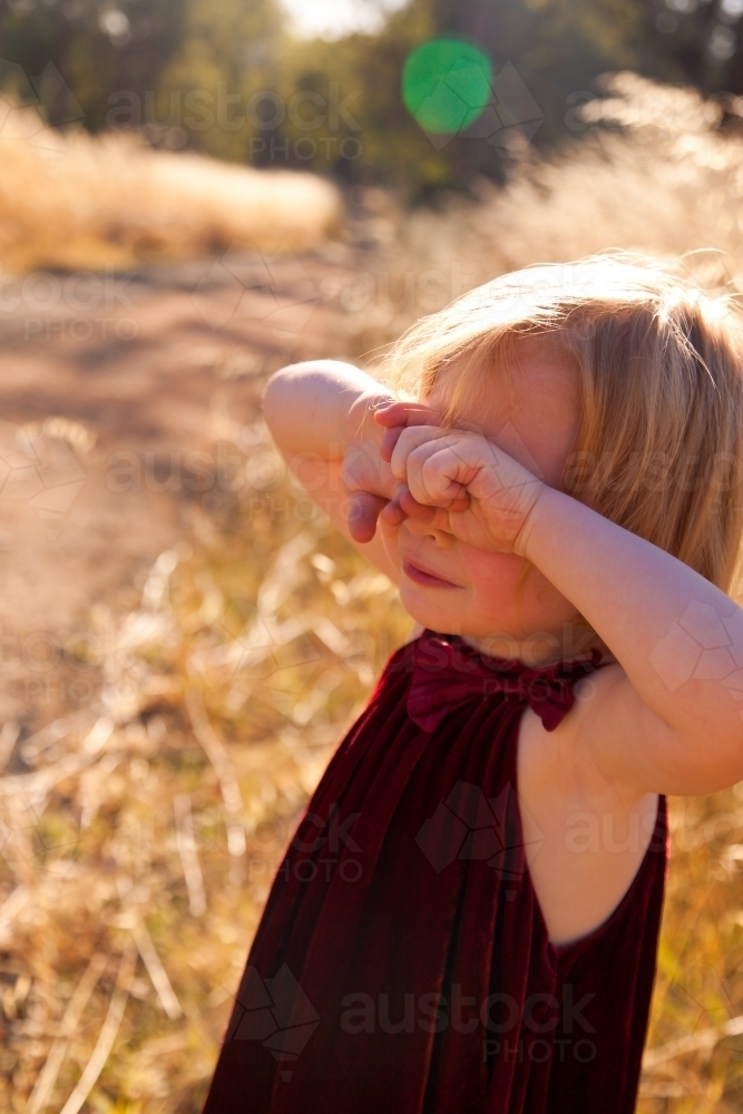 Young girl holding holding her hands over her eyes in summer light - Australian Stock Image