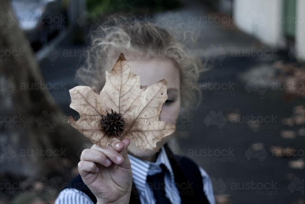 Young girl holding leaf in front of face - Australian Stock Image