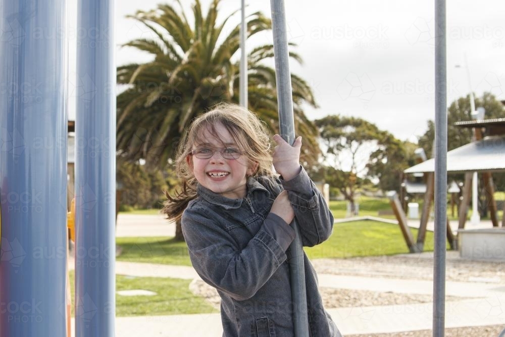 Young girl holding onto pole at playground - Australian Stock Image