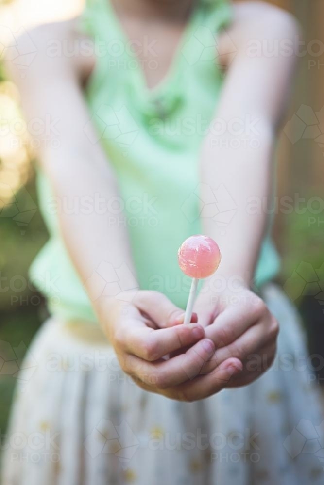 Young girl holding or offering a pink lollipop to camera - Australian Stock Image