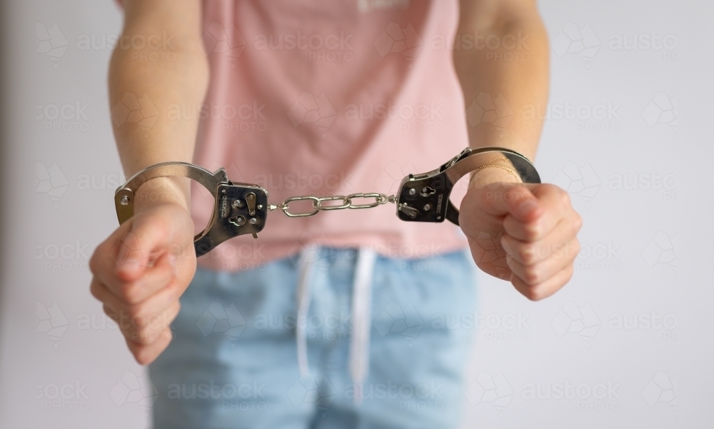 young girl holding out arms with handcuffs around wrists - Australian Stock Image