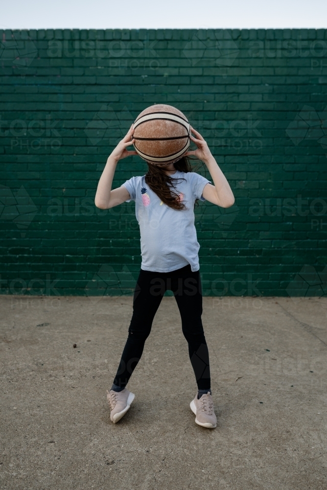 Young girl holding up a basketball in front of her face - Australian Stock Image