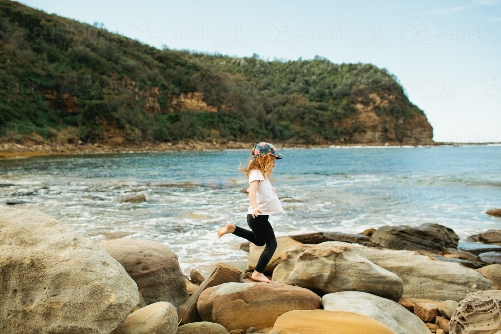 Young girl hopping across rocks at the beach - Australian Stock Image