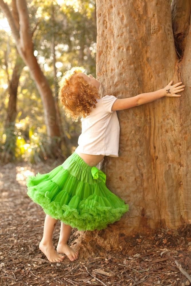 Young girl hugging a tree wearing a green tutu skirt - Australian Stock Image