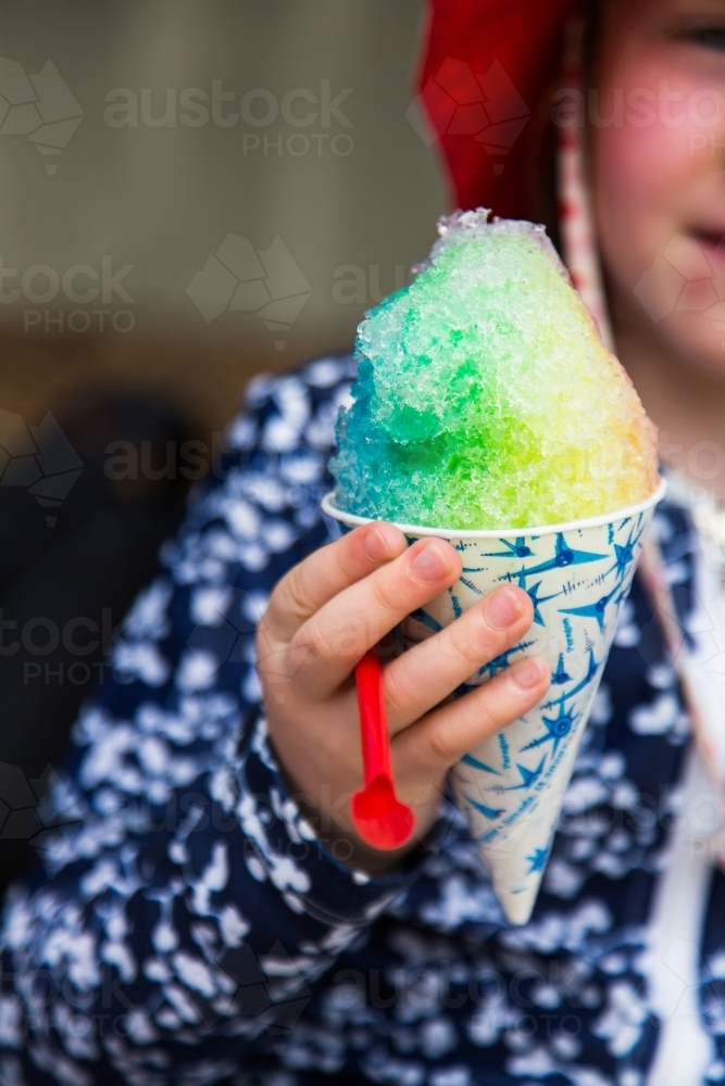 Young girl in a rashie holding a rainbow coloured snow cone - Australian Stock Image