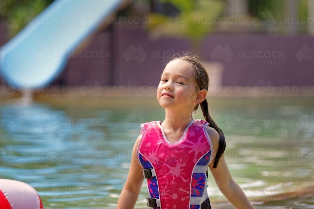Young girl in a swimming pool playing with a ball wearing a swim vest - Australian Stock Image