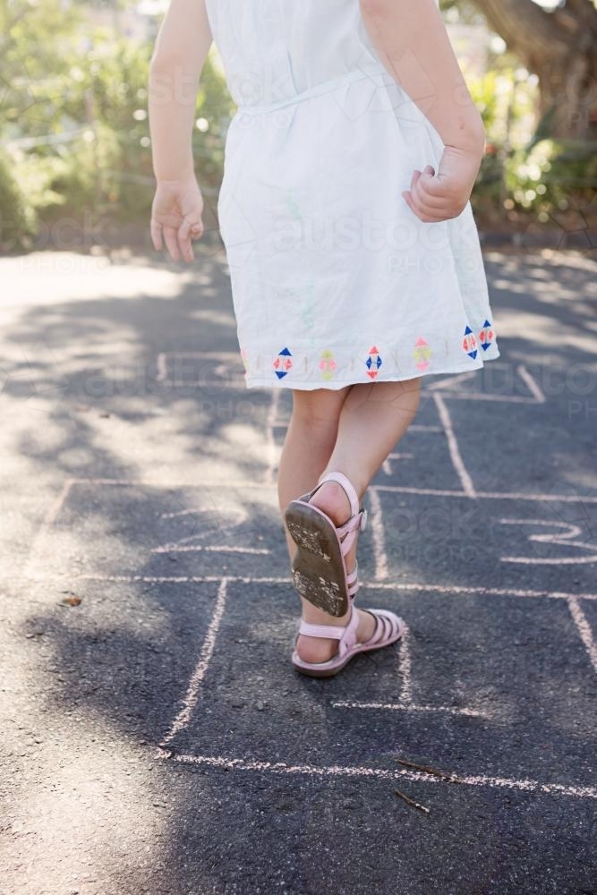 Young girl in a white dress playing hopscotch in the street - Australian Stock Image