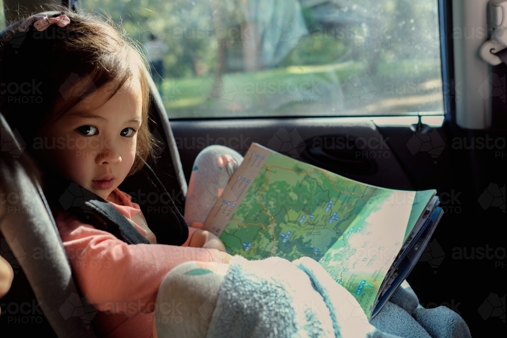 Young girl in car seat reading map on road trip - Australian Stock Image