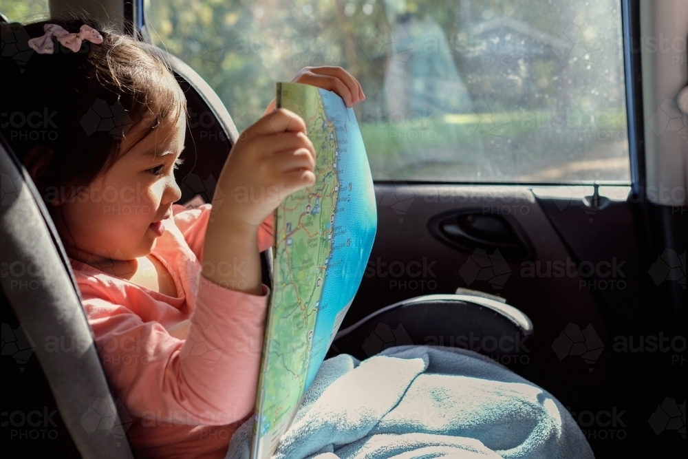Young girl in car seat reading map on road trip - Australian Stock Image