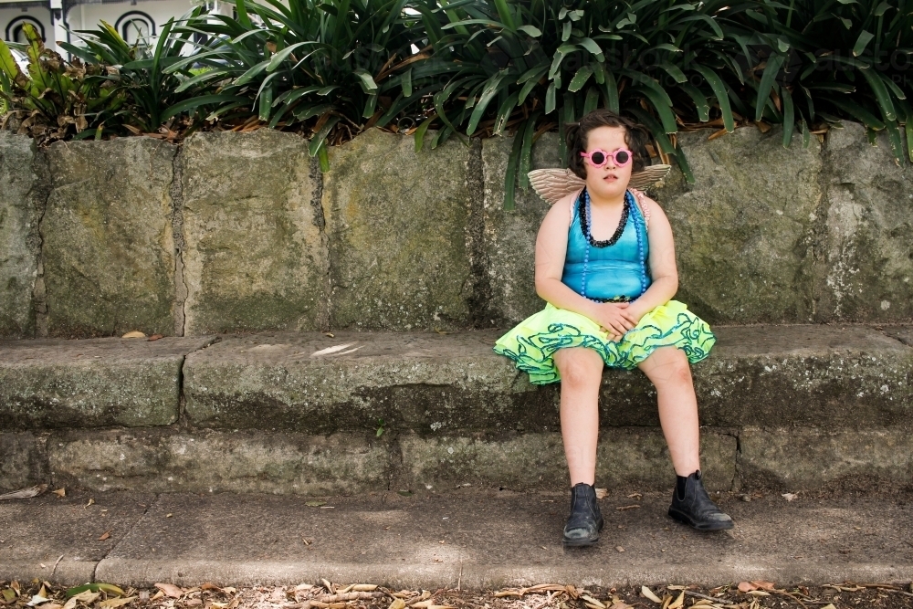 Young girl in gaudy dress-up sitting on a sandstone bench seat - Australian Stock Image