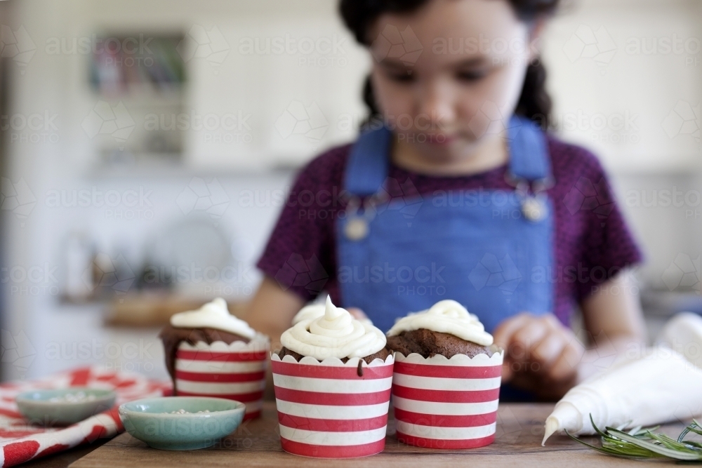 Young girl in kitchen at home decorating Christmas cupcakes - Australian Stock Image